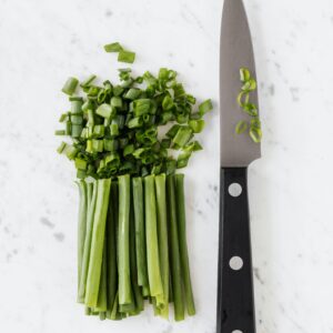 Top view of chopped scallions with a knife on a marble background, perfect for food blogs and culinary content.